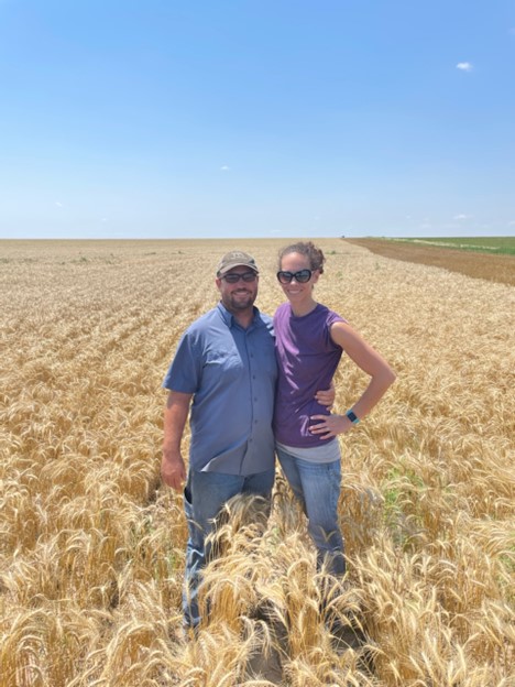 Jay Young in a blue shirt and blue jeans standing in a wheat field with his wife in a purple shirt and jeans